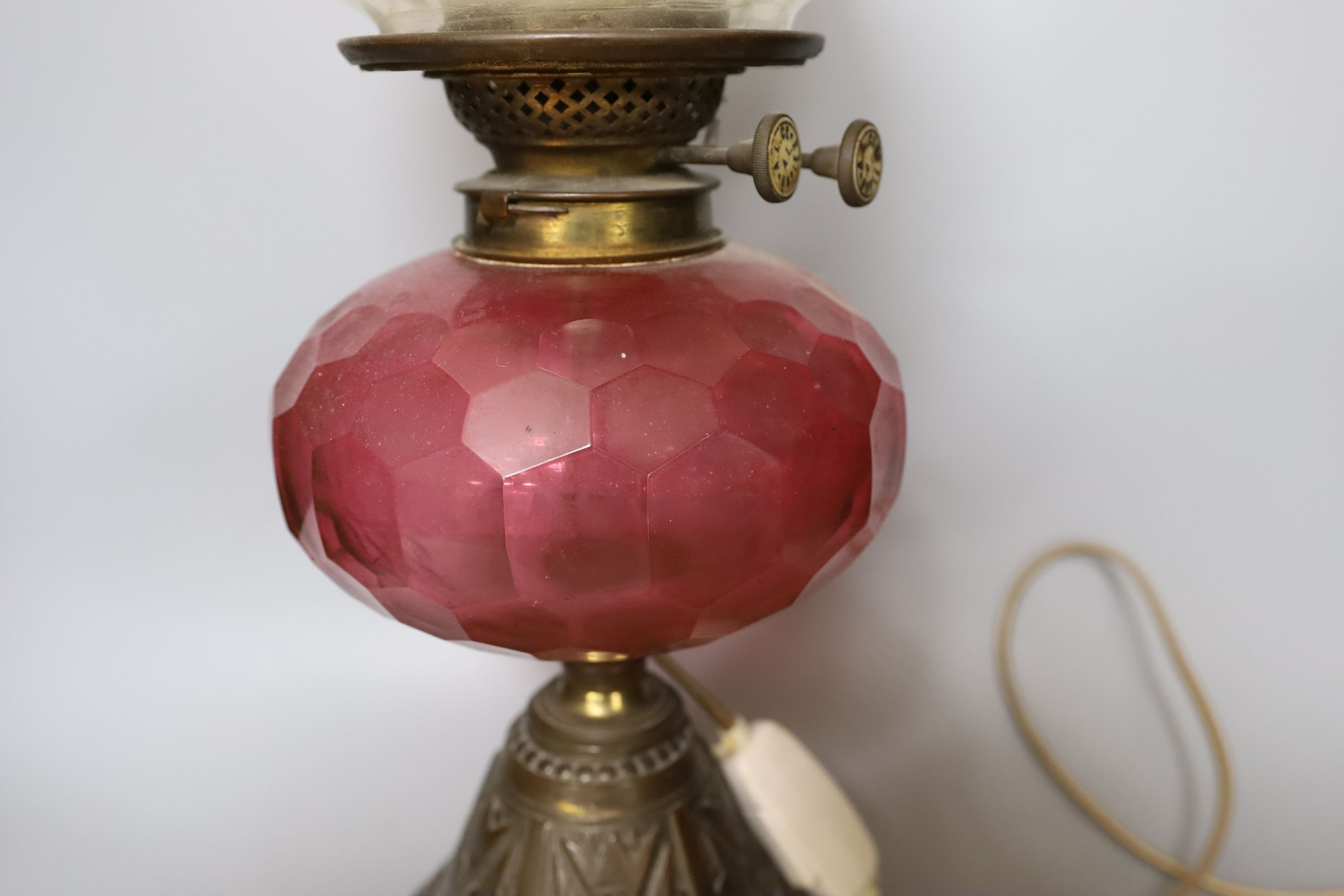 An Edwardian oil lamp with ruby glass font, later inverted to electricity, 57 cms high including funnel.